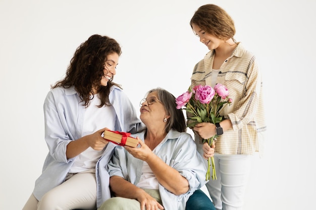 Happy adult european woman and teen girl give gift flowers to elderly lady