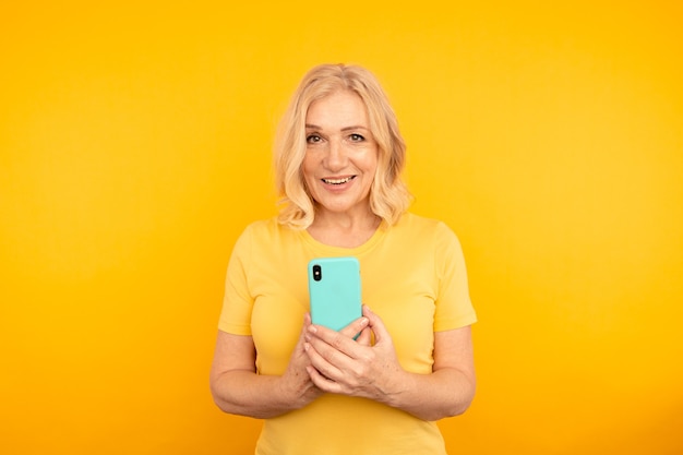 Happy adult female with blue mobile on the yellow background