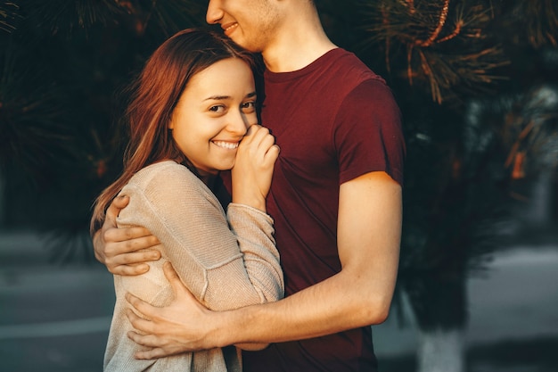 Happy adult lovely female looking at camera smiling while leaning her head on her boyfriend chest outside while dating.