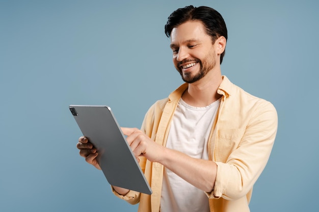 青い背景に隔離されたデジタルタブレットでブラウジングをしている幸せな成人男性