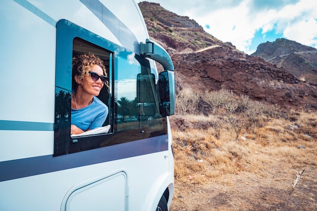 Happy adult woman smile and enjoy travel destination inside her\
camper van cheerful female people enjoy travel with camper van\
concept of van life and people renting motor home off grid\
parking