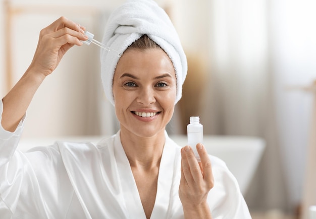 Happy adult woman using moisturizing facial serum copy space