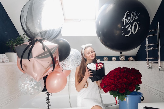 Happy adult woman with flowers and air balloons in bathroom