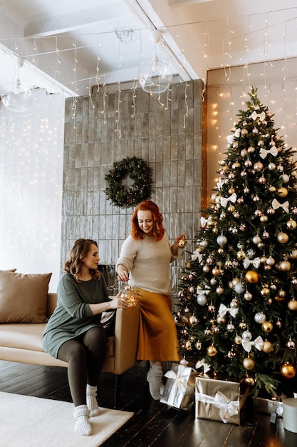 Happy adult women in casual clothes decorating a Christmas tree at home