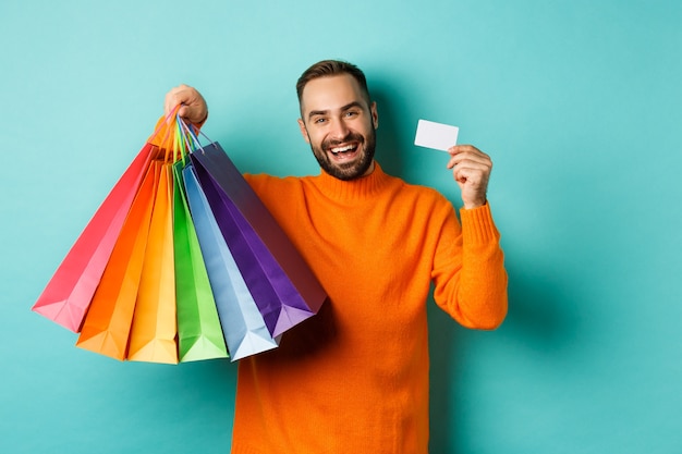 Happy aduly man showing credit card and shopping bags, standing