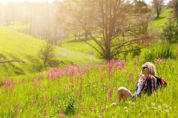 La donna felice dell'avventuriero si trova sul pendio verde della montagna tra i rododendri rosa in fiore e guarda in lontananza. viaggio epico in montagna. angolo ampio.