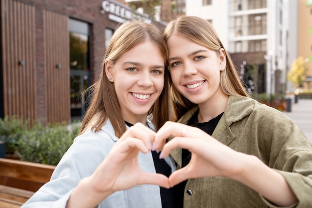 Happy affectionate twin girls making shape of heart with hands