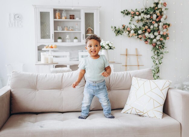 A happy African American black boy is standing on a sofa in the living room