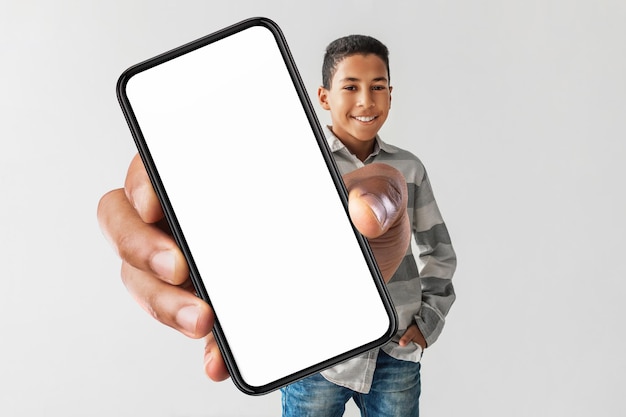 Happy african american boy holding huge smartphone on gray background