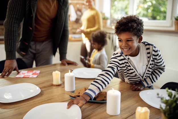 Happy African American boy setting the table for family lunch during holidays
