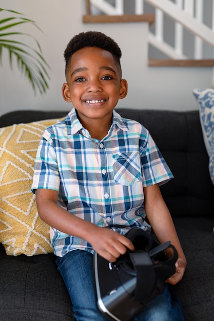 Happy african american boy sitting on sofa and holding vr headset