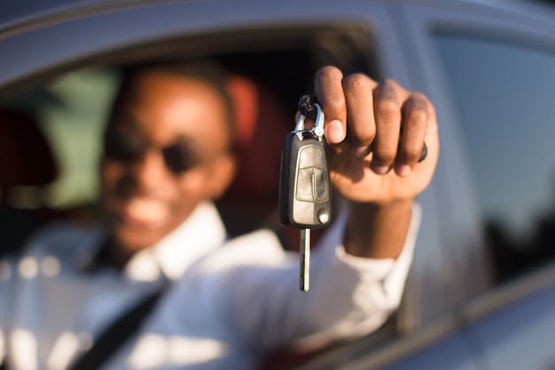 Happy African American in a car with a key, in the summer