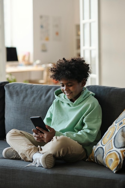 Happy African American child in casualwear sitting on couch in living room