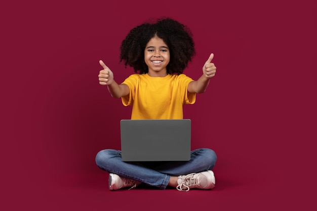 Happy african american child using laptop showing thumb up