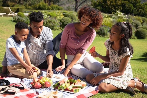 Happy african american couple with son and daughter outdoors, having picnic in sunny garden. family enjoying quality free time together.