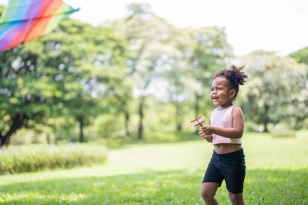 Happy African American cute little girl enjoys playing with kite in park on holidays in summer