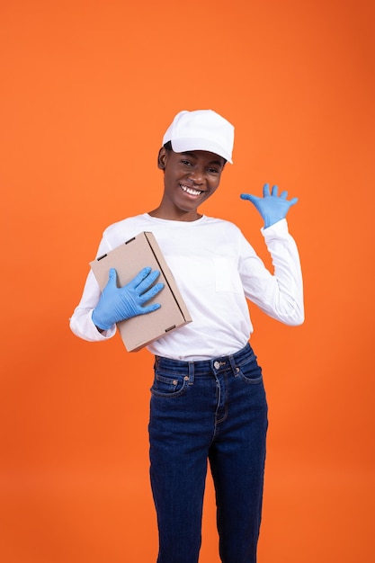 Happy African American delivery girl with a box on orange background with copy space