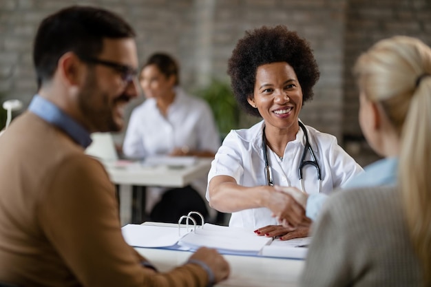 Felice medico afroamericano che stringe la mano a una coppia dopo un appuntamento medico in clinica