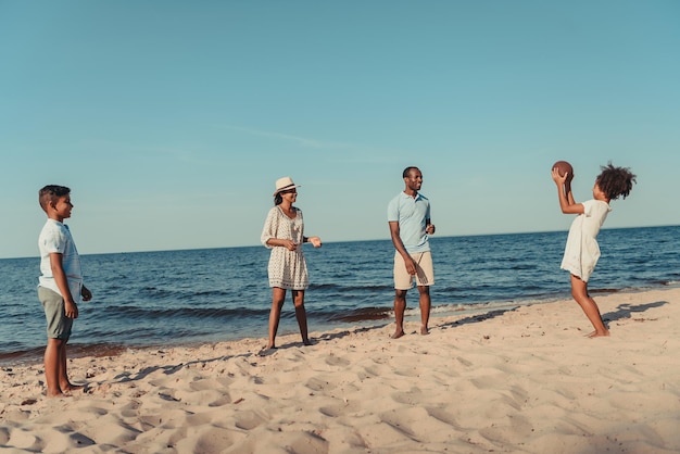 Felice famiglia afroamericana che gioca con il pallone da rugby sulla spiaggia