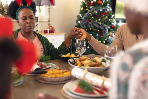 Photo happy african american family praying before having christmas meal. christmas, family time and celebration concept.