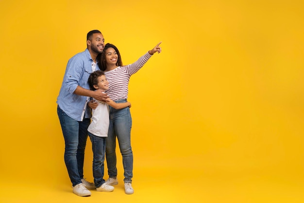 Happy african american family of three pointing finger aside at copy space