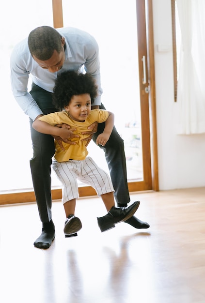 행복한 아프리카계 미국인 아버지는 퇴근 후 아이가 아버지의 신발을 신고 놀고 있는 동안 어린 아들을 집으로 데려다 줍니다.