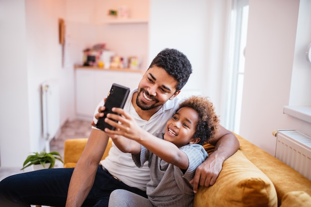 Padre e figlia afroamericani felici che fanno un selfie a casa.