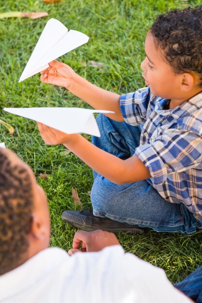 Foto felice padre afroamericano e figlio di razza mista che giocano con aeroplani di carta nel parco