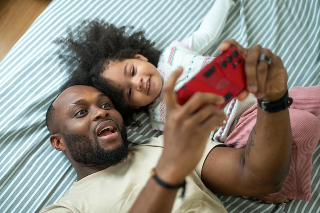 Happy African American father playing with his girl in bedroom at home