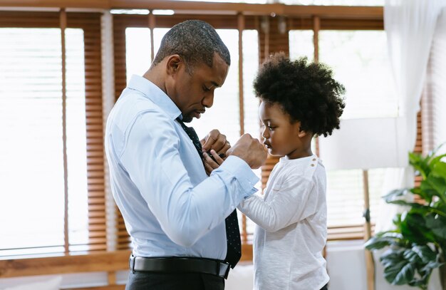 Happy African American Father and son spend time together Little boy helping his father tie necktie at home