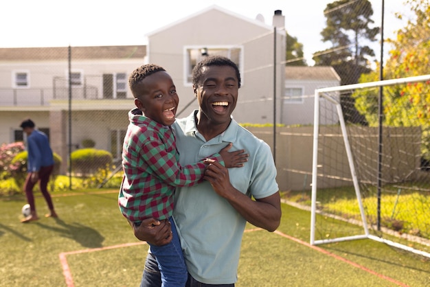 Photo happy african american father and son spending time together and playing football outside