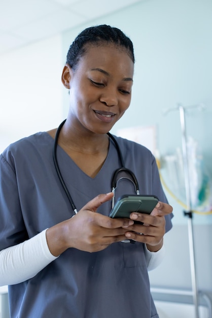 Happy african american female doctor using smartphone in hospital room