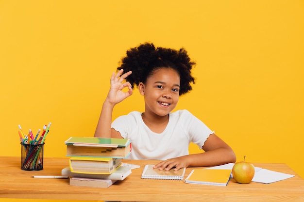 Happy African American female schoolgirl sitting at desk and stretching arm up during class Back to school concept