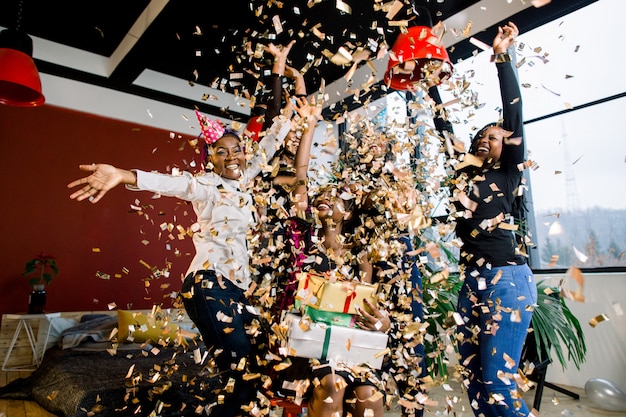 Ragazze felici degli amici dell'afroamericano sotto i coriandoli di caduta alla festa di compleanno