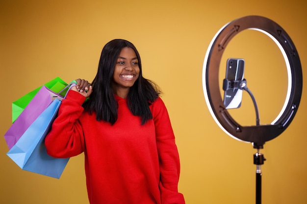 Happy African American girl in a red hoodie with colorful bags on her shoulder a ring lamp