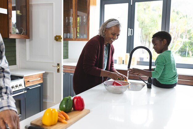 Happy african american grandmother and grandson washing vegetables in kitchen slow motion