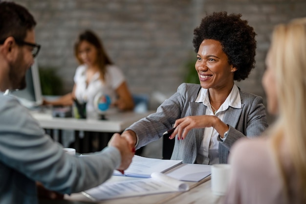 Happy African American insurance agent greeting her clients and handshaking with them in the office