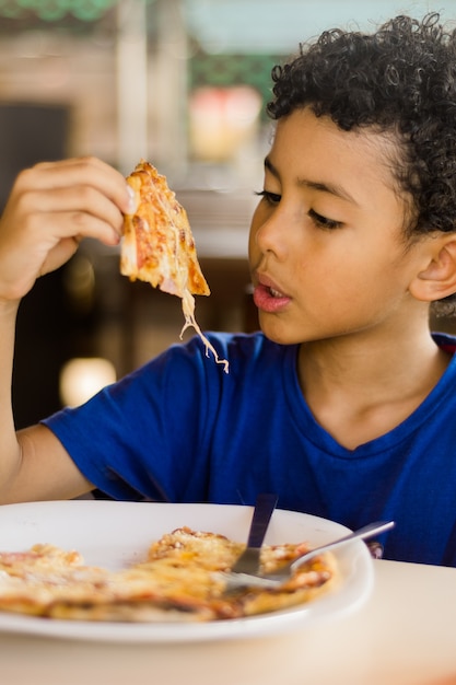 Happy african american kid eating pizza.