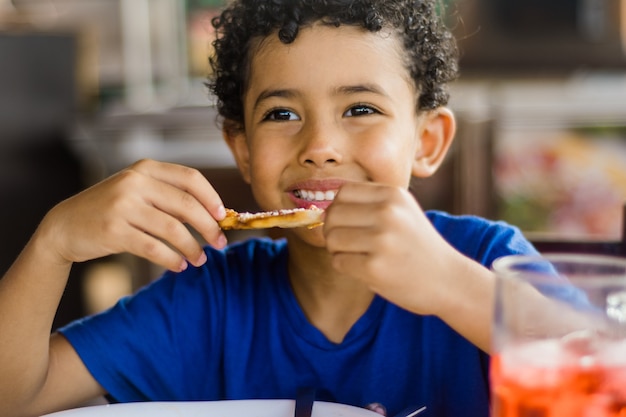 Happy african american kid eating pizza.