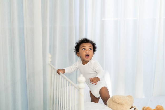 행복한 아프리카 계 미국인 작은 아기는 침대의 머리를 올라