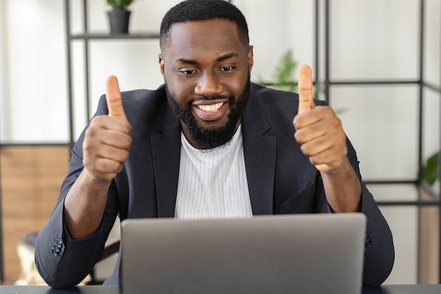 행복한 아프리카계 미국인 프리랜서 또는 사업가가 노트북을 행복하게 보고 있고, 좋은 메시지를 받거나 좋은 거래를 했습니다.