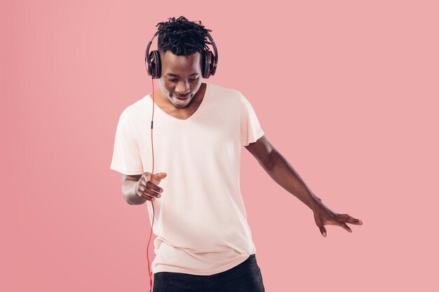 Happy African-American man in headphones listening to music on pink background