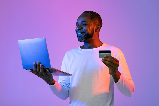 Happy african american man holding computer and credit card