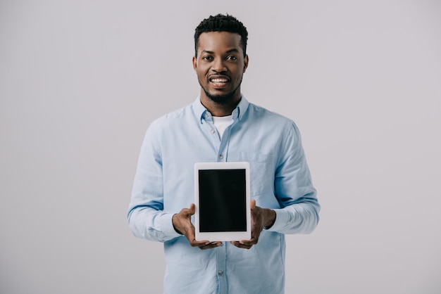 Happy african american man holding digital tablet with blank screen isolated on grey