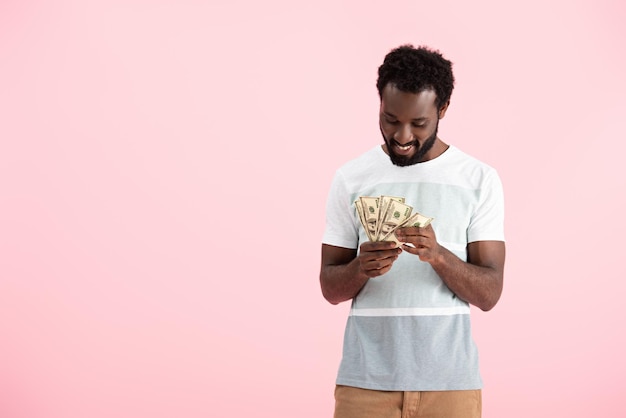 Photo happy african american man holding dollars banknotes isolated on pink