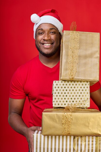 Счастливый афроамериканец в шляпе Санты улыбается, потому что получил много подарков на Рождество