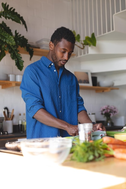 幸せなアフリカ系アメリカ人男性がキッチンに立って夕食を作ります。家で一人で充実した時間を過ごす。