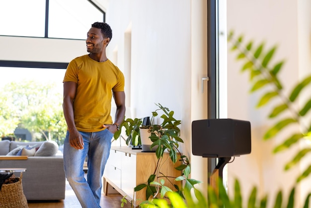 Happy african american man standing, smiling and looking away in sunny living room. Lifestyle, wellbeing, happiness and domestic life, unaltered.