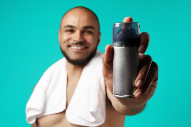 Happy african american man with towel holding shaving foam on turquoise