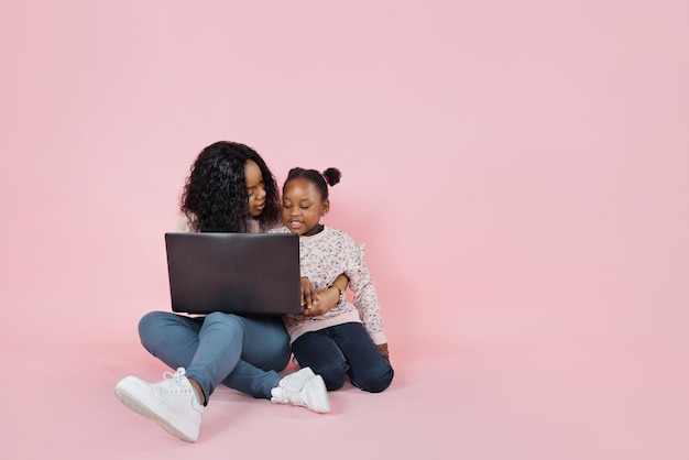 행복한 아프리카계 미국인 엄마와 작고 귀여운 딸이 노트북을 사용하여 함께 시간을 보냅니다.